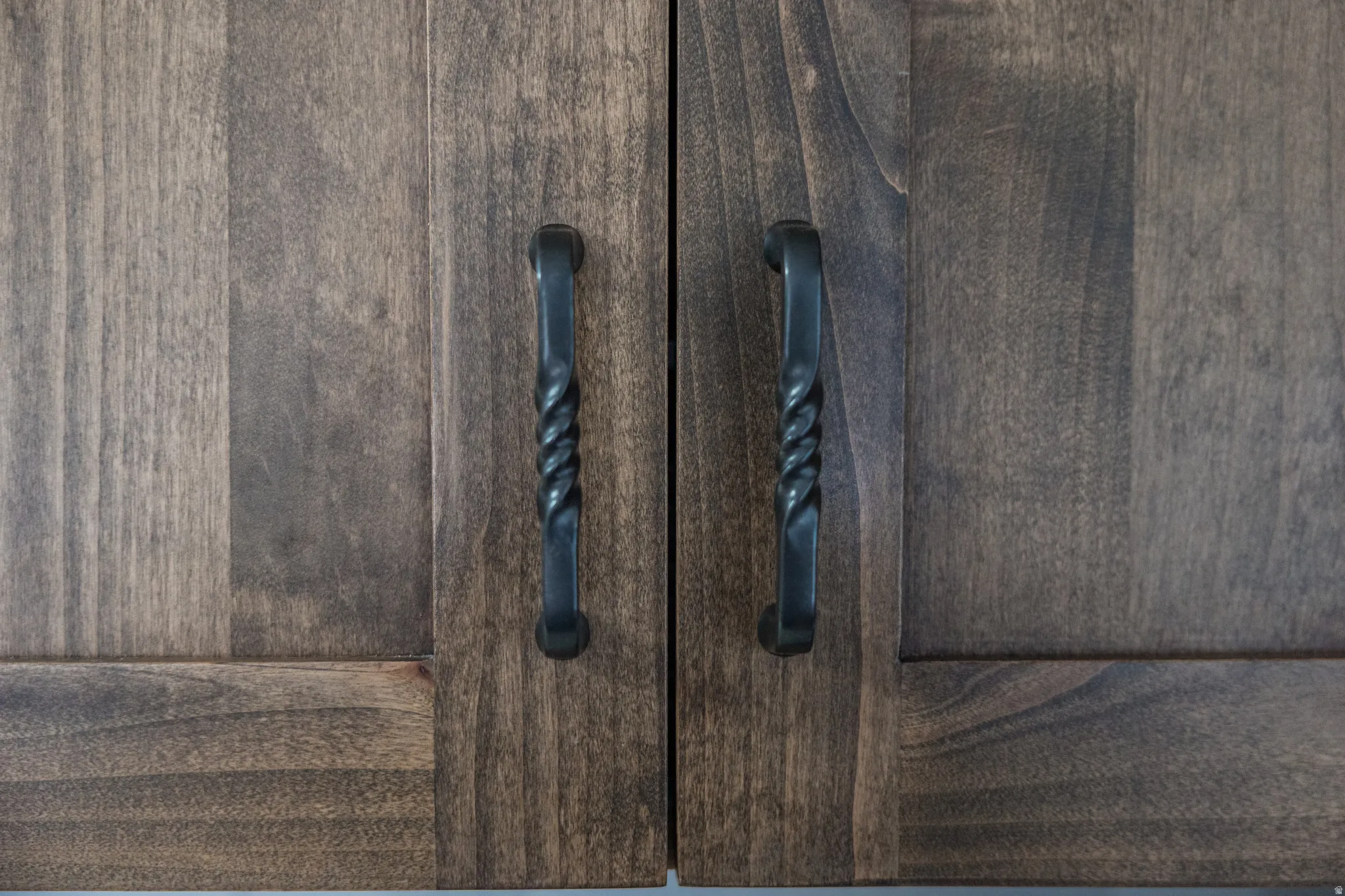 Wood-finish cabinet doors featuring matching dark hardware with a twisted design
