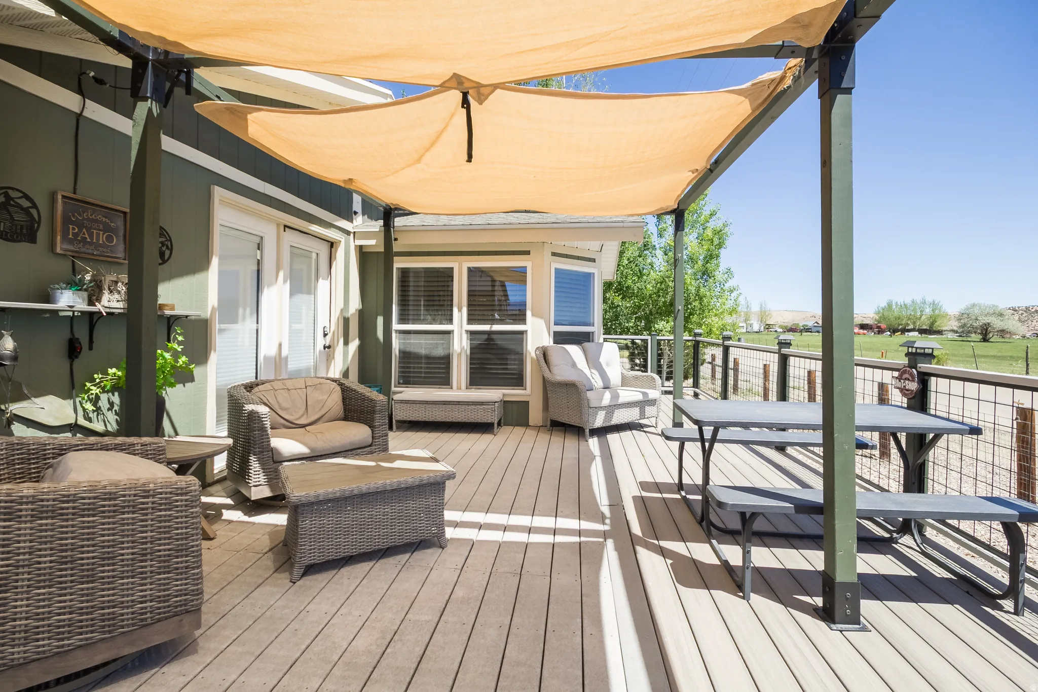 Expansive wood-finish deck featuring a partial overhead sunshade, decorative railing, and double French doors