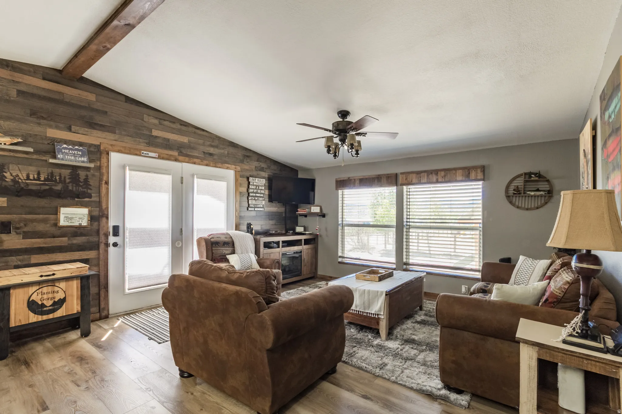 Spacious living area featuring wood-finish flooring, a vaulted ceiling with exposed wood beam, and a ceiling fan with integrated lighting
