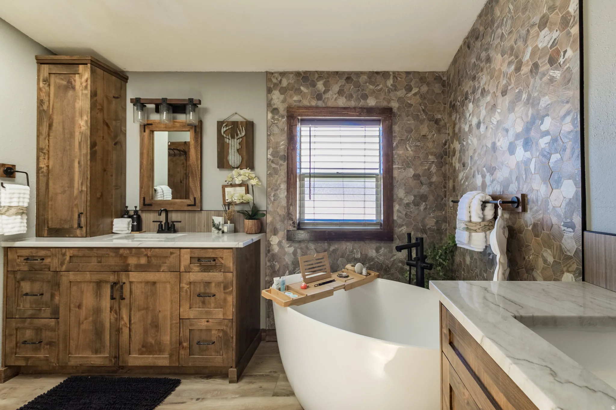 Bathroom featuring a freestanding soaking tub, wood-finish vanity with a light countertop, and a tiled accent wall