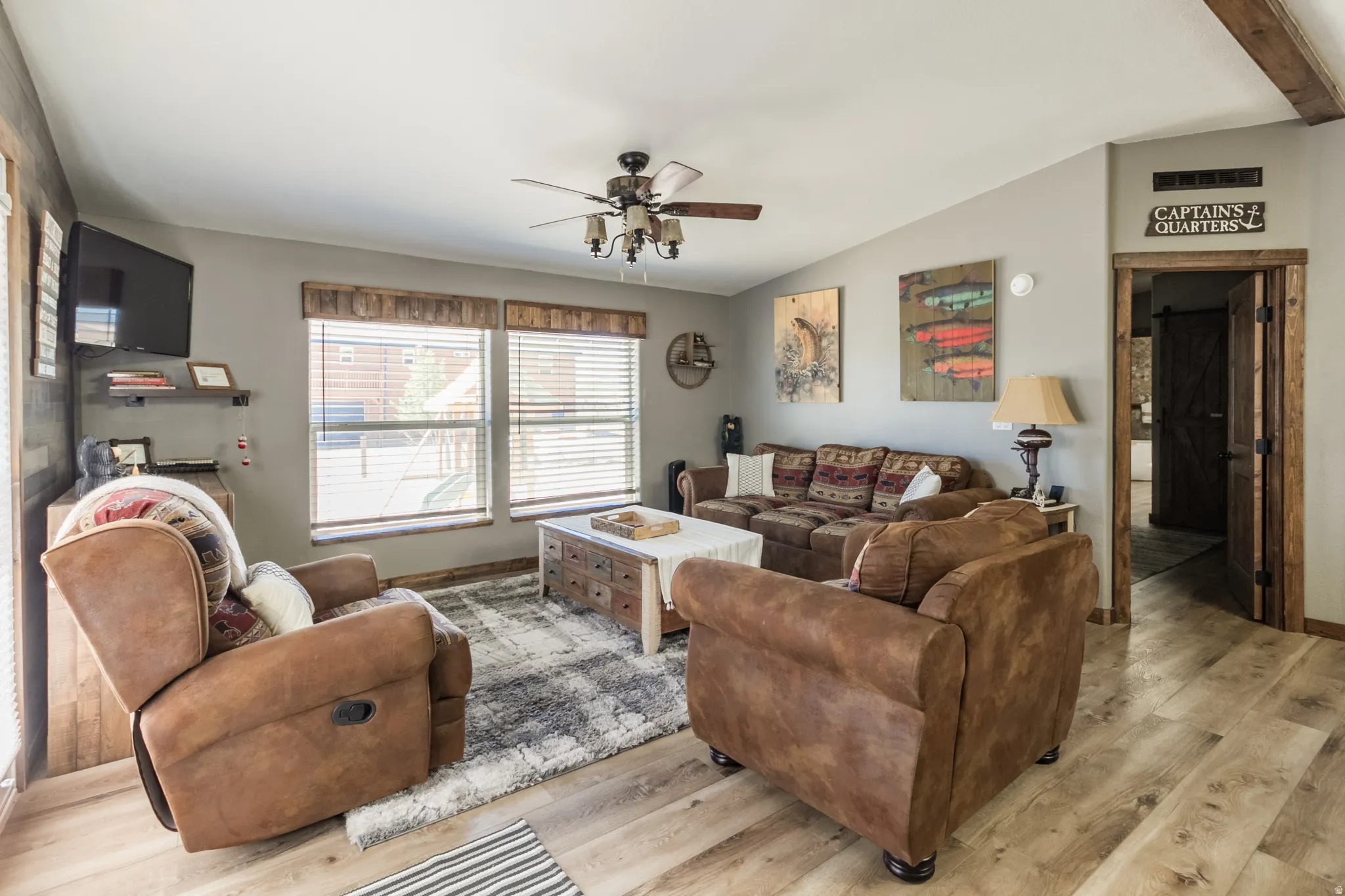 Living area featuring light wood-finish flooring, neutral wall paint, and a ceiling fan with integrated lighting