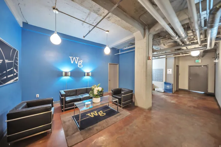 Lobby area featuring a blue accent wall with ambient sconce lighting, suspended pendant lights, exposed industrial-style ceiling ductwork, and concrete flooring