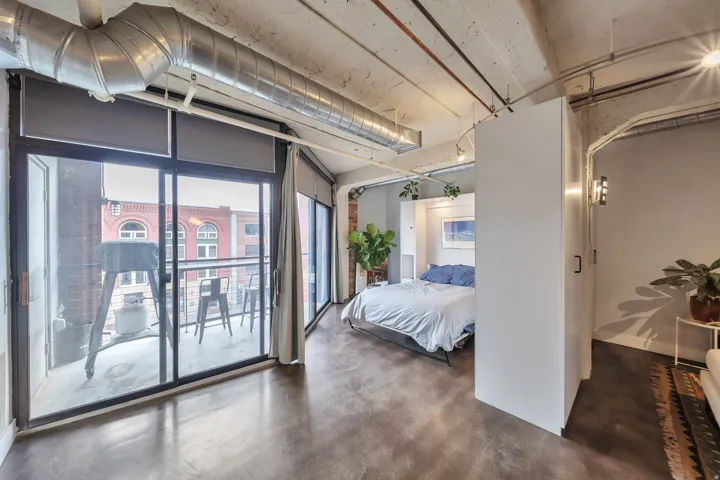 Spacious interior featuring a full-width sliding glass door to the balcony, exposed ductwork, concrete flooring, and a partial wall dividing the space
