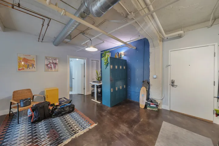 Interior space featuring exposed ductwork and conduit, concrete ceilings, dark-finish flooring, and a vibrant blue accent wall with integrated shelving