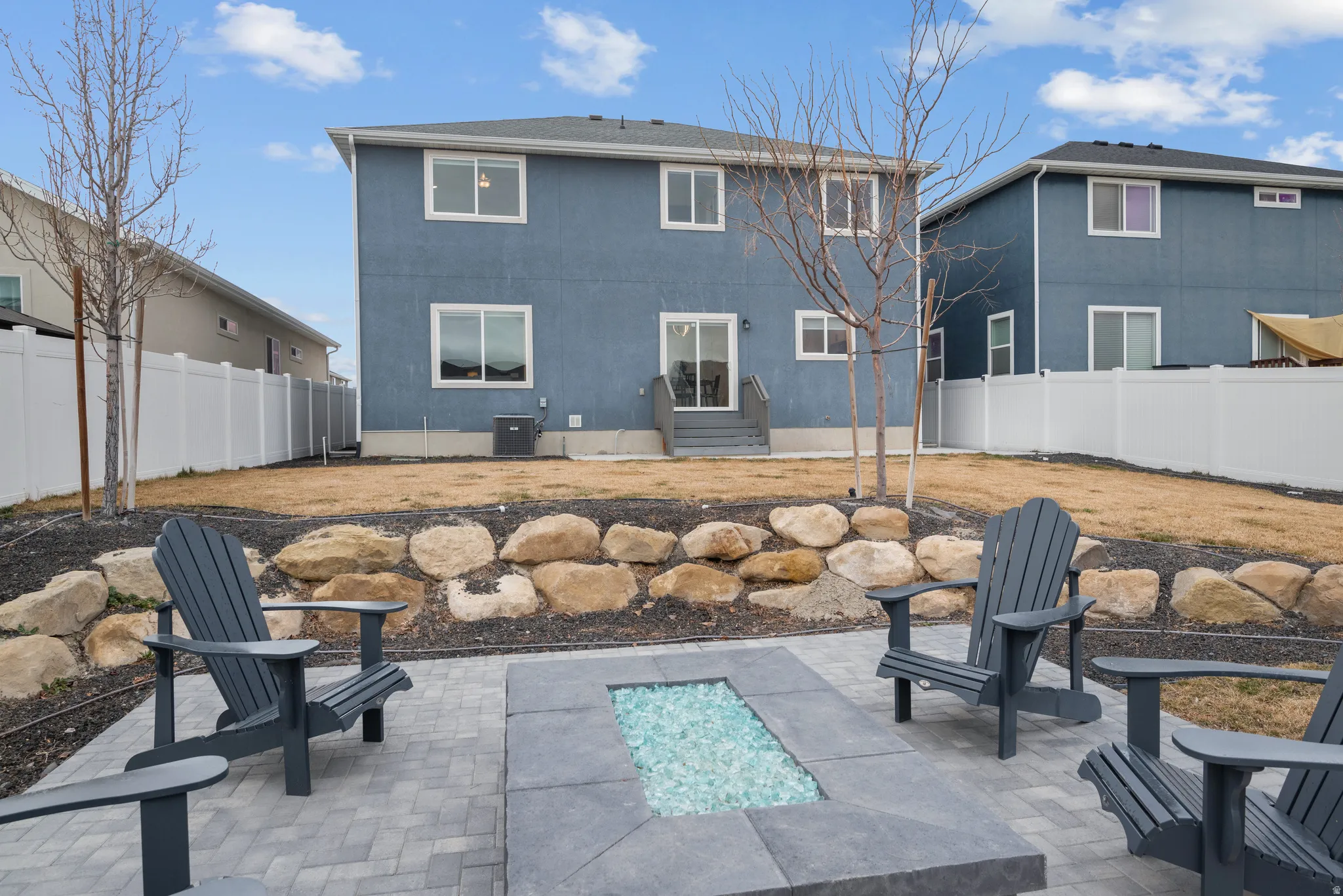 Paver patio with a built-in fire pit featuring clear fire glass, surrounded by a rock retaining wall and a terraced backyard
