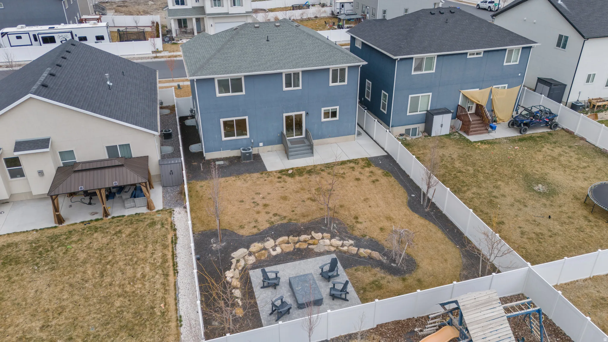Rear exterior featuring a spacious yard, concrete patio, and a stone-lined fire pit area
