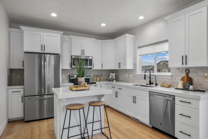 Modern kitchen featuring white shaker cabinetry, stainless steel appliances, quartz counter tops, tile backsplash, and LVP flooring