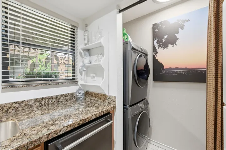 Laundry area featuring a stacked washer and dryer, granite-style countertop, undermount sink, and a built-in shelf