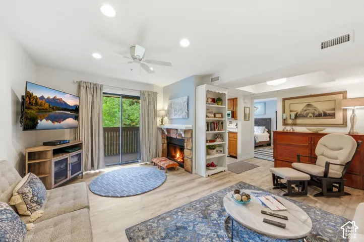 Open-concept living area featuring wood-finish flooring, a stone-faced fireplace, a ceiling fan, recessed lighting, and a sliding glass door opening to an outdoor space