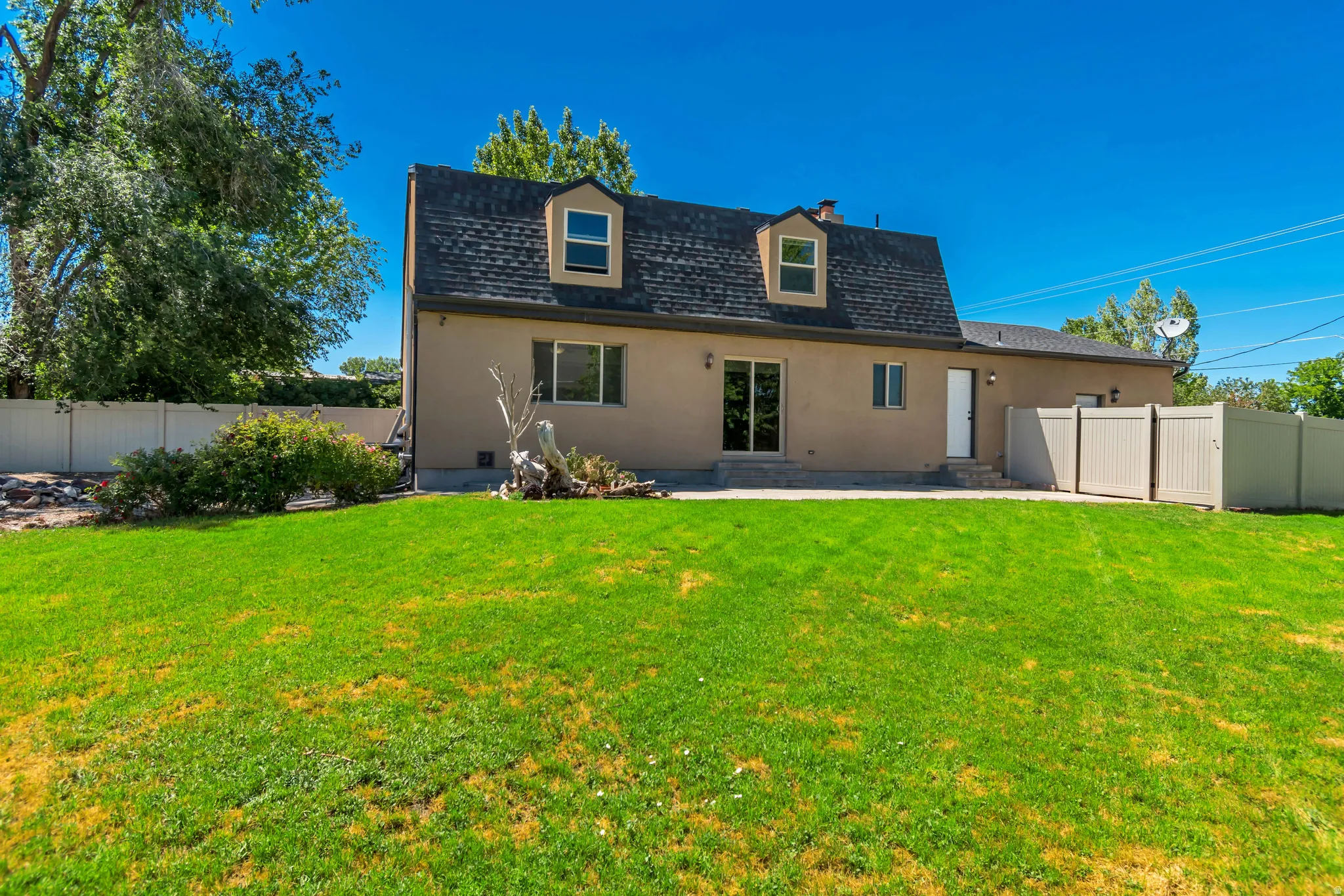Expansive rear yard featuring a manicured lawn, full vinyl privacy fencing, a concrete patio, and mature perimeter trees