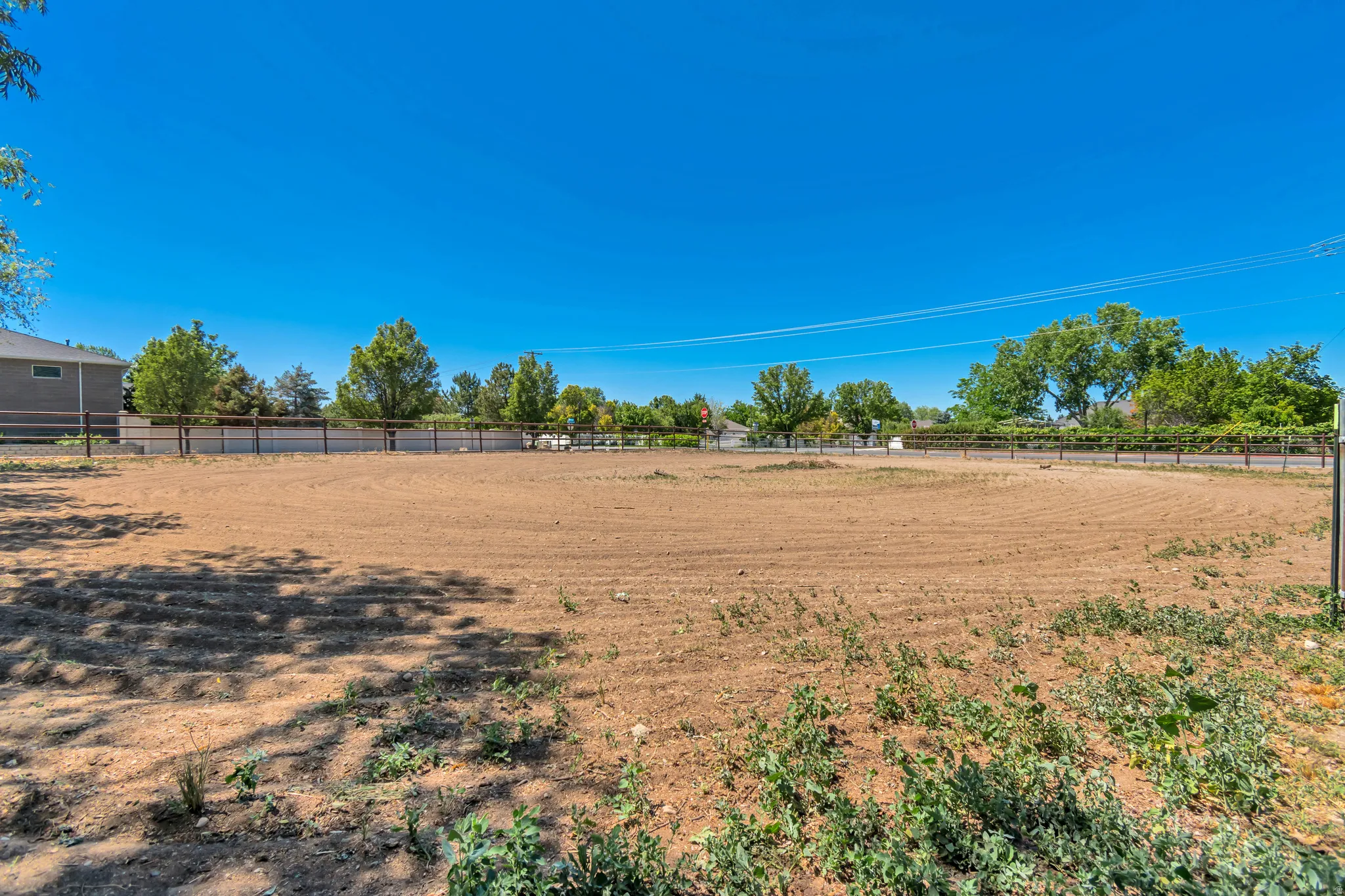 Expansive cleared lot featuring a perimeter fence and mature trees along the boundary