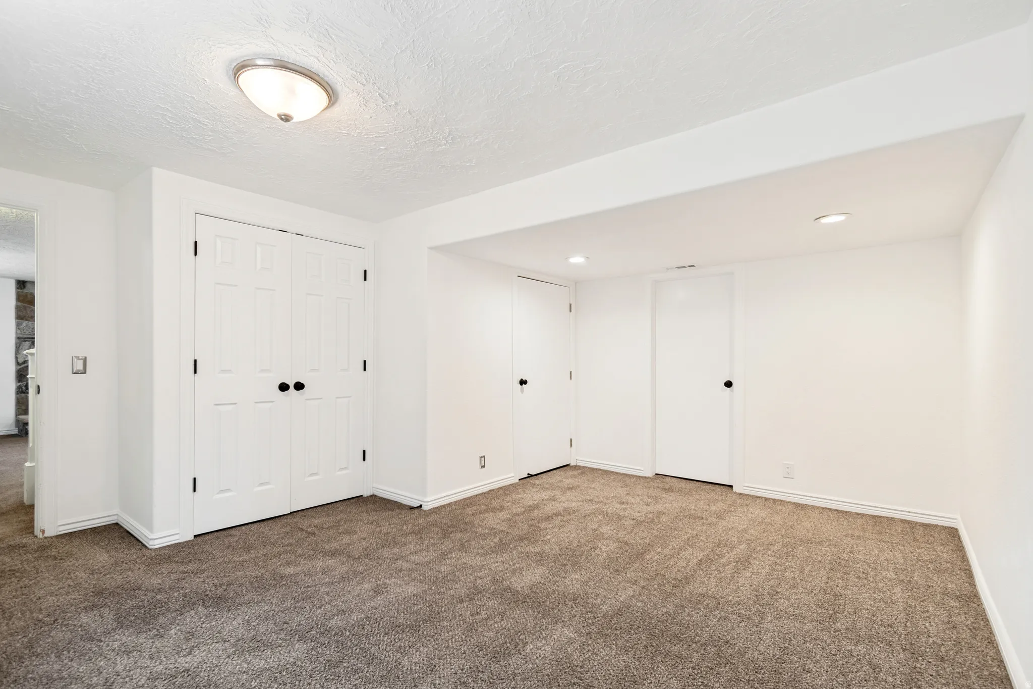 Spacious room featuring new carpeting, crisp white walls, multiple recessed lights, and a flush mount ceiling fixture