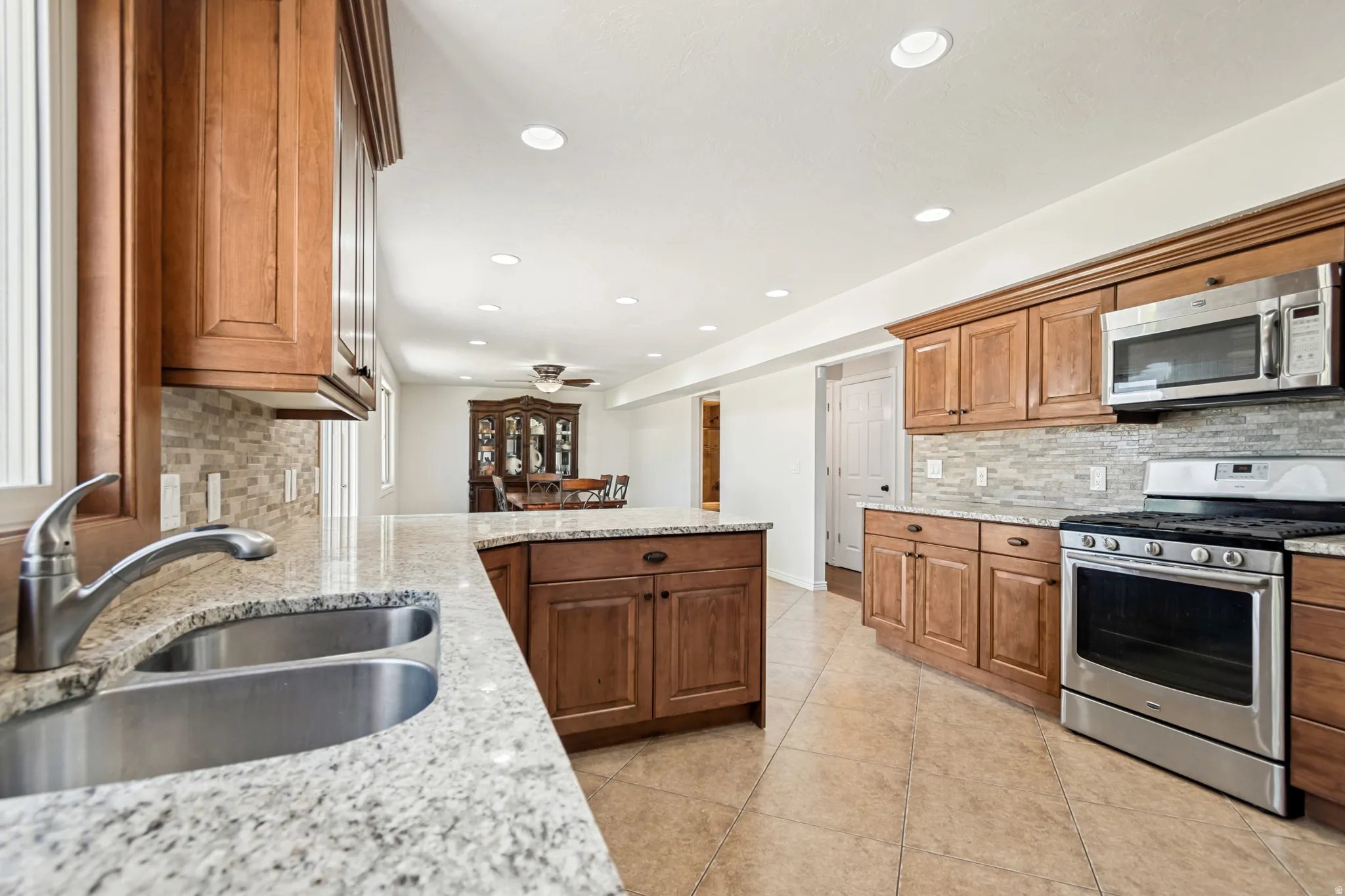 Kitchen featuring wood cabinetry, light-toned granite-style countertops, stainless steel appliances, a double basin sink, and an extended island