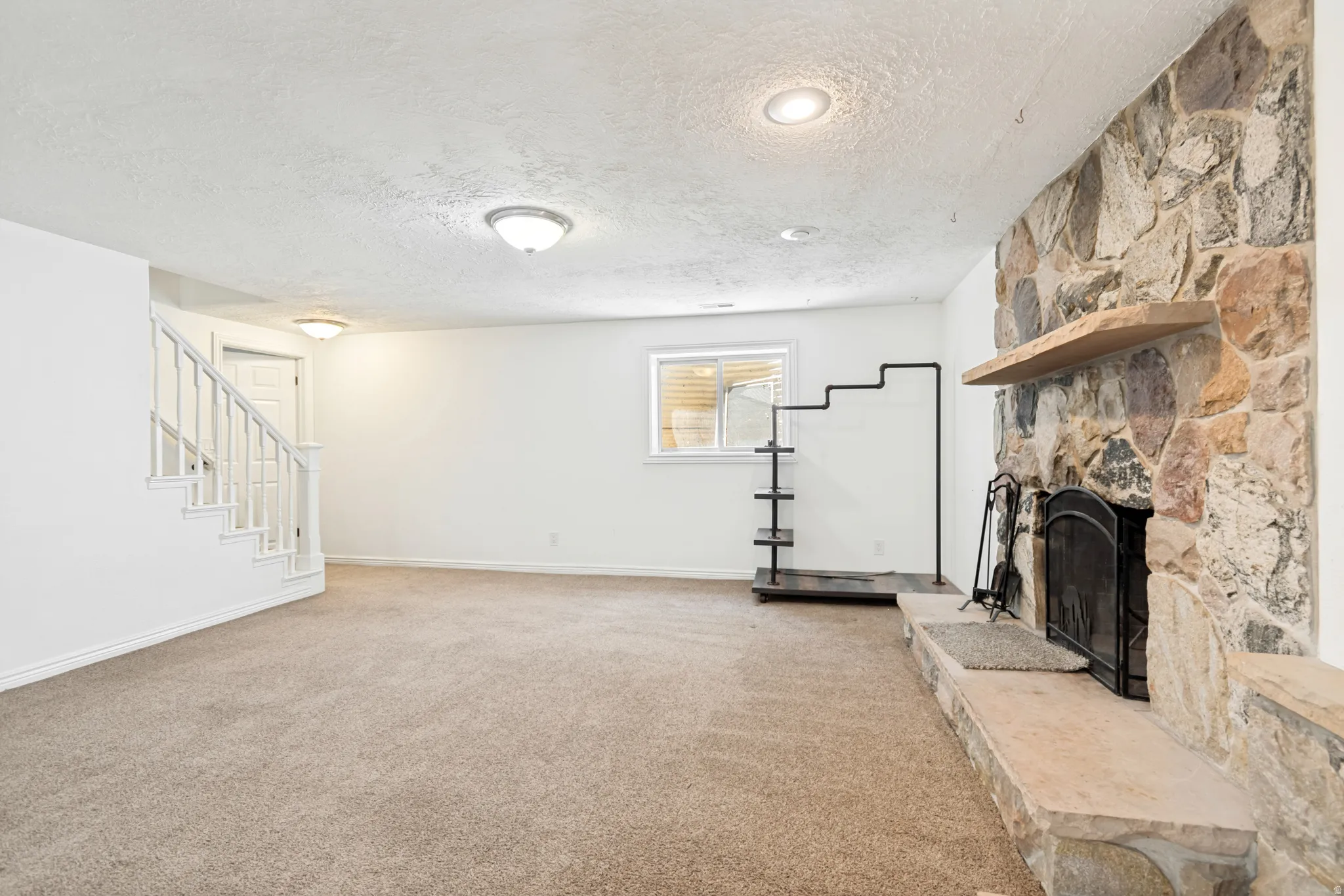 Spacious room featuring a large stone fireplace with a hearth and mantel, neutral carpet flooring, and white painted walls