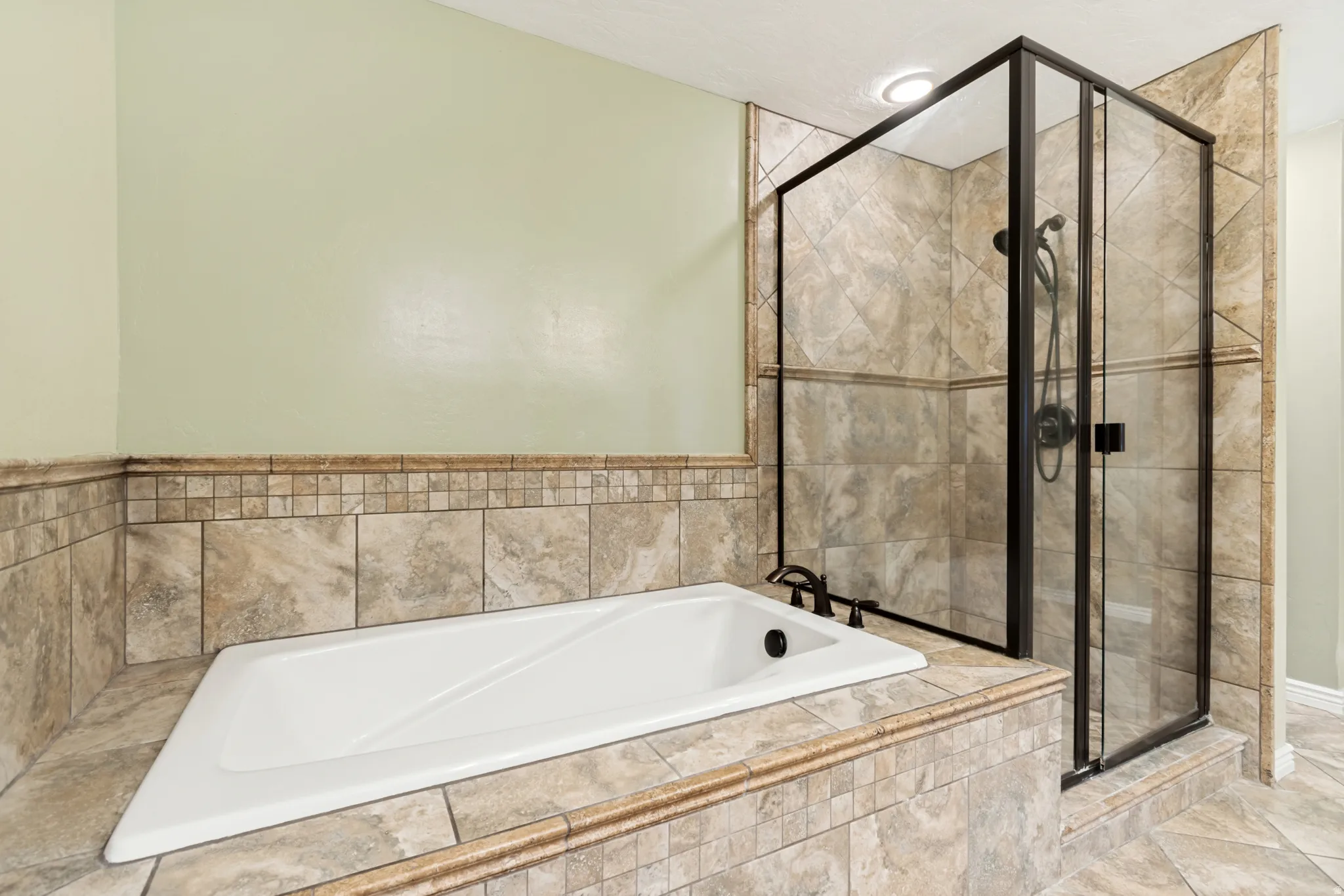 Soaking tub with bronze fixtures, surrounded by neutral-toned tile and a mosaic accent border