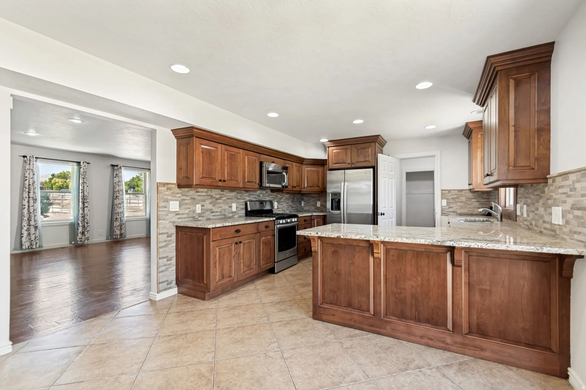 Kitchen featuring wood cabinetry, granite countertops, tile backsplash, stainless steel appliances, and recessed lighting