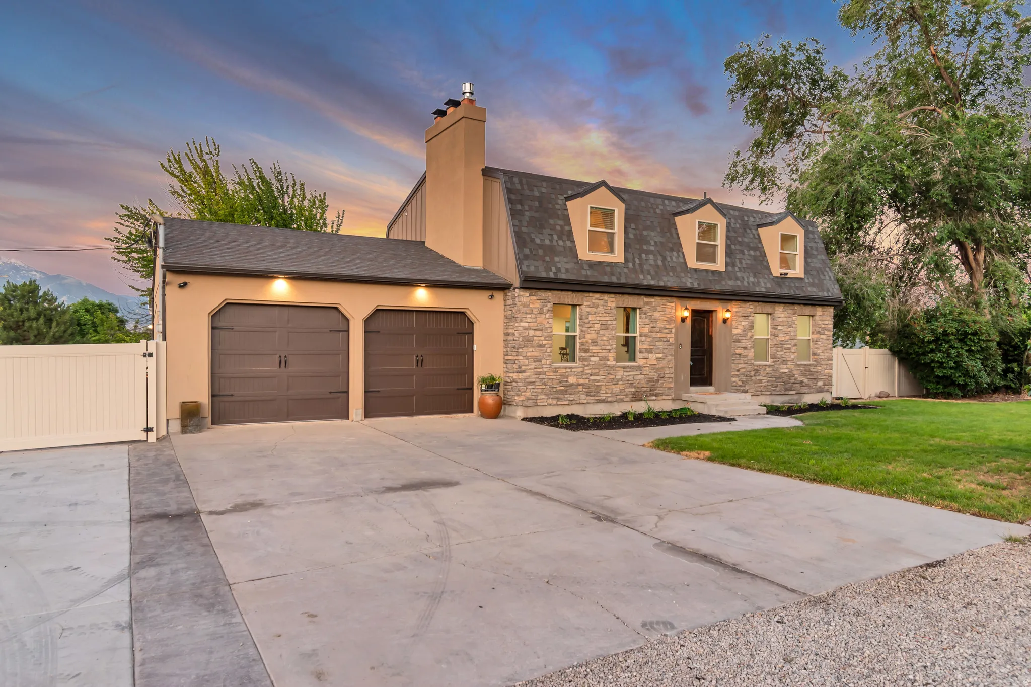 Stone veneer and stucco exterior with dormer windows, a two-car garage, established front landscaping, and a concrete driveway