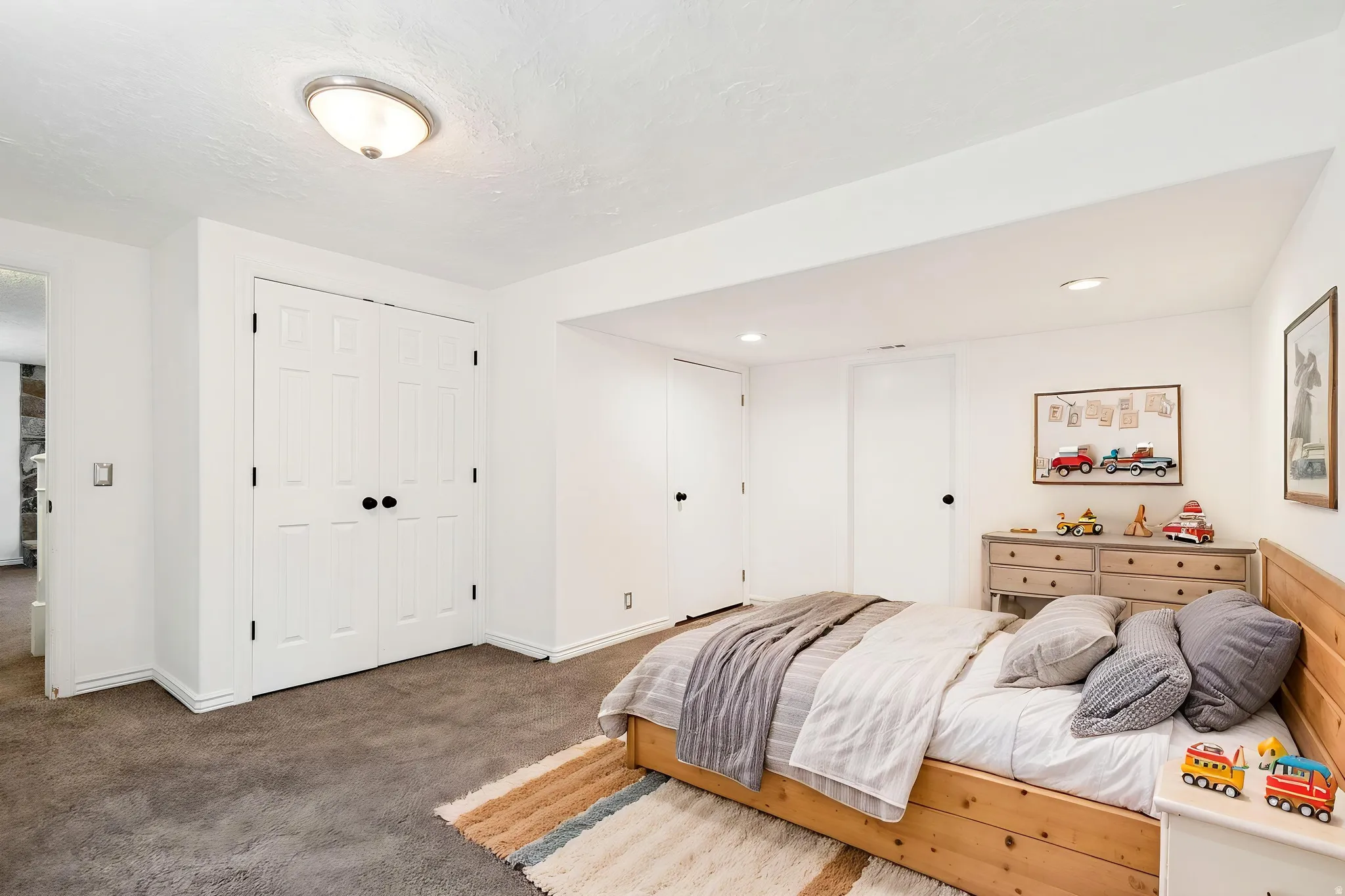 Virtually staged - Carpeted room featuring white walls, a flush-mount ceiling light fixture, and white bi-fold closet doors with black hardware