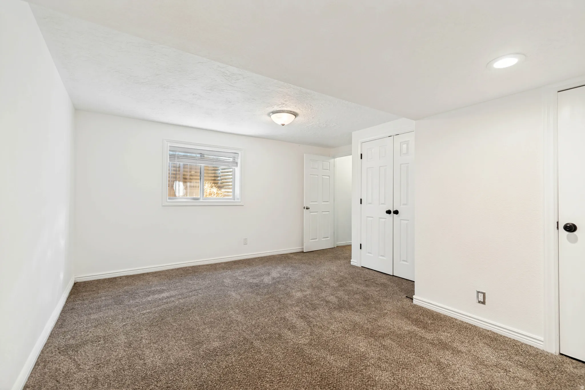Carpeted room with white walls, a single window with horizontal blinds, and a built-in closet with bi-fold doors