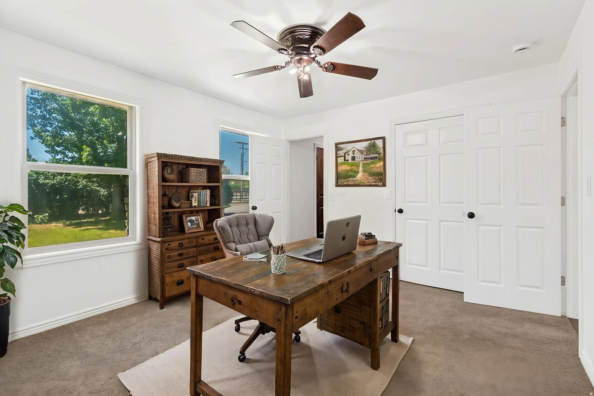 Virtually staged as an office - Bright room featuring a ceiling fan with integrated lighting, two windows, and textured carpet flooring