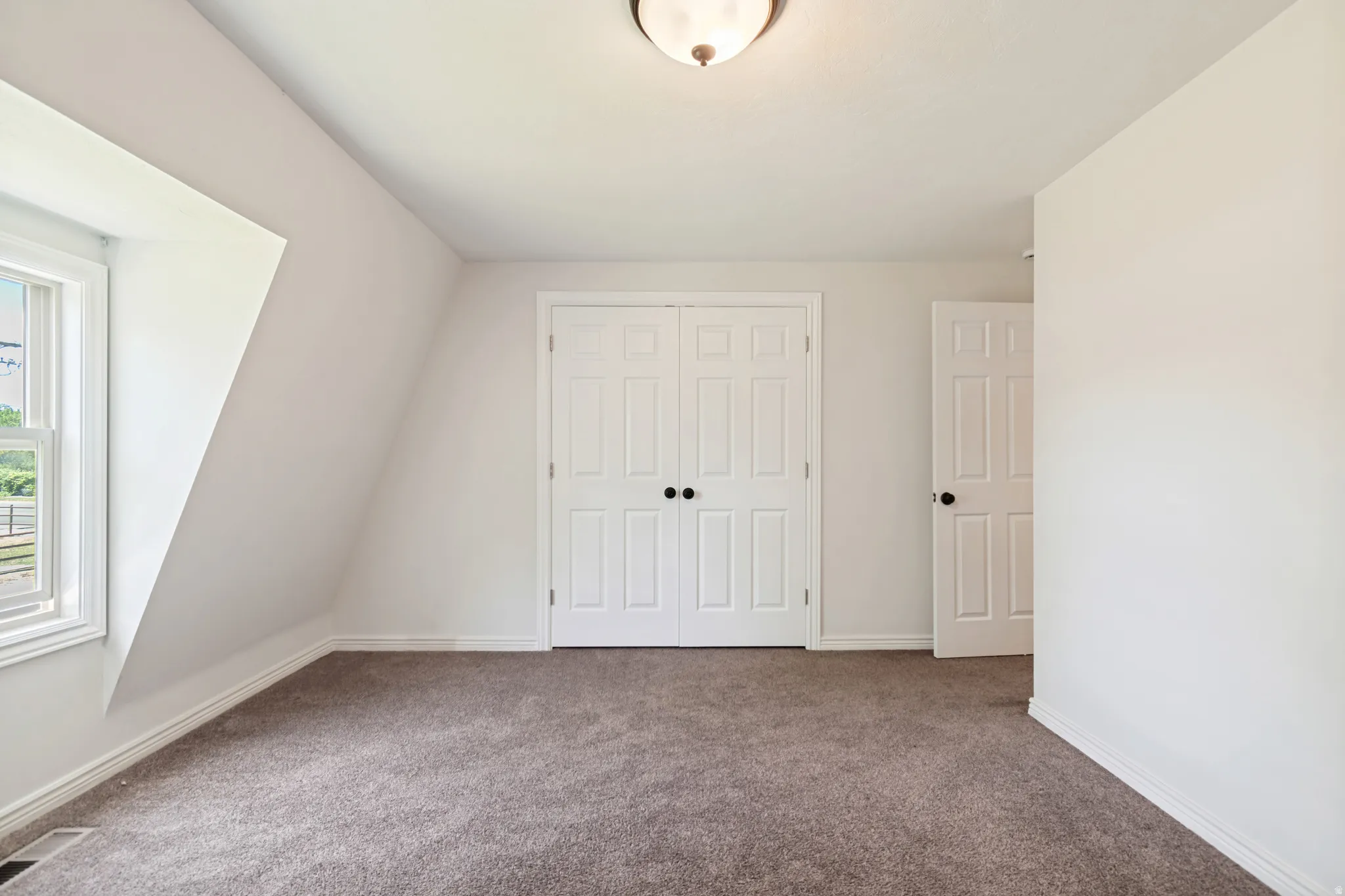 Carpeted room with a pitched ceiling and a double-hung window