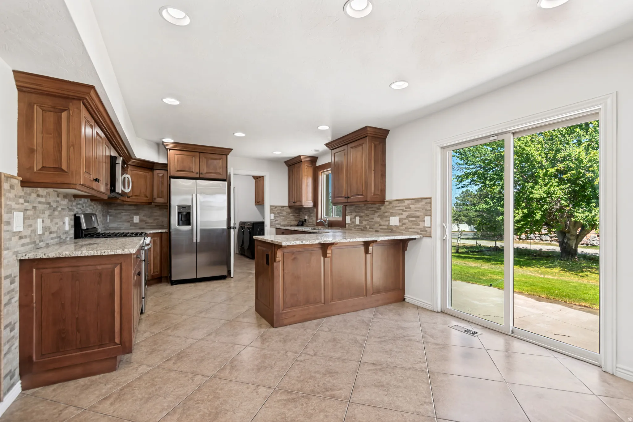 Spacious kitchen featuring warm wood cabinetry, granite countertops, stainless steel appliances, a tiled backsplash, and recessed lighting
