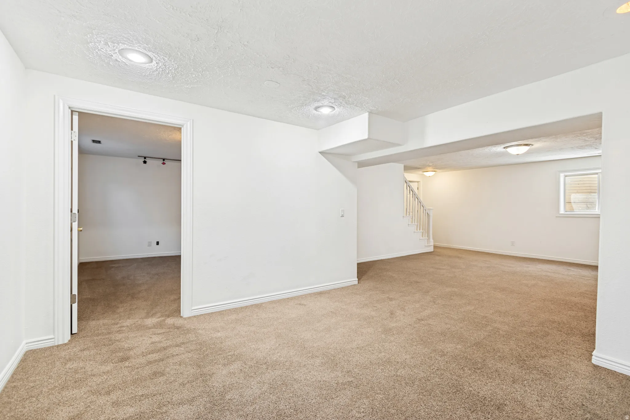 Spacious carpeted room featuring white painted walls, recessed lighting, and a doorway leading to an additional area