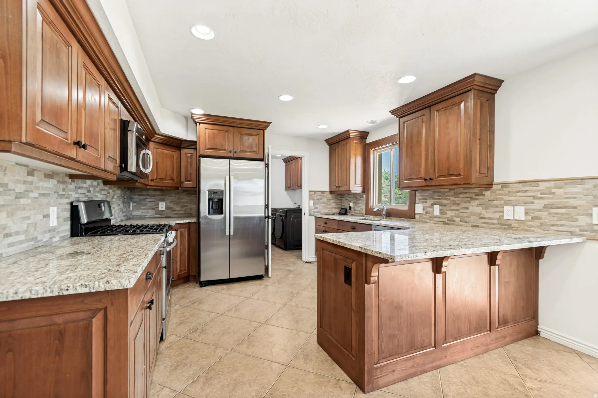 Kitchen featuring wood cabinetry, light-toned countertops, a full stainless steel appliance suite, mosaic tile backsplash, and recessed lighting
