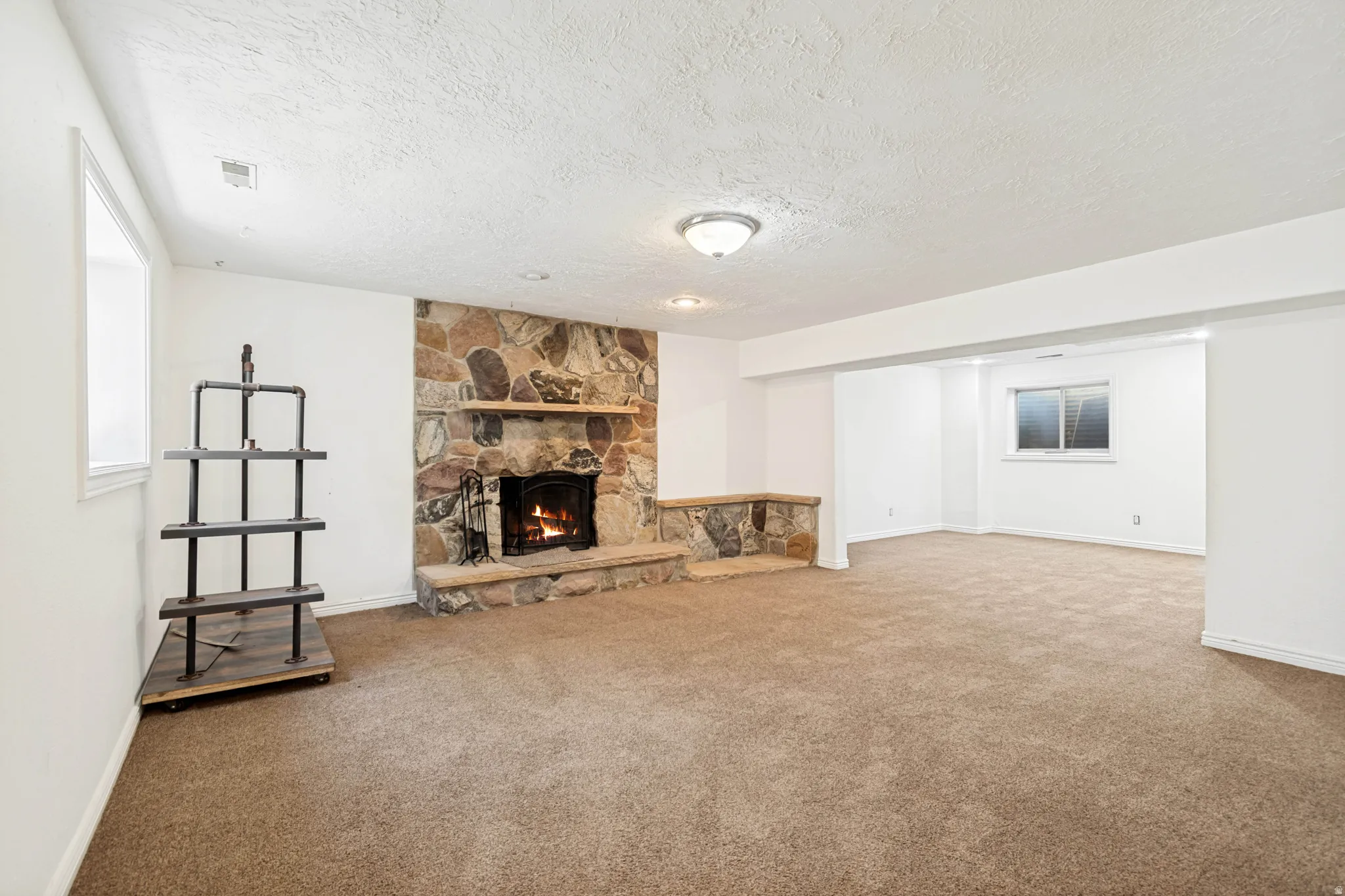 Spacious room featuring a stone fireplace with a wood mantle, carpet flooring, recessed lighting, and a built-in stone half-wall