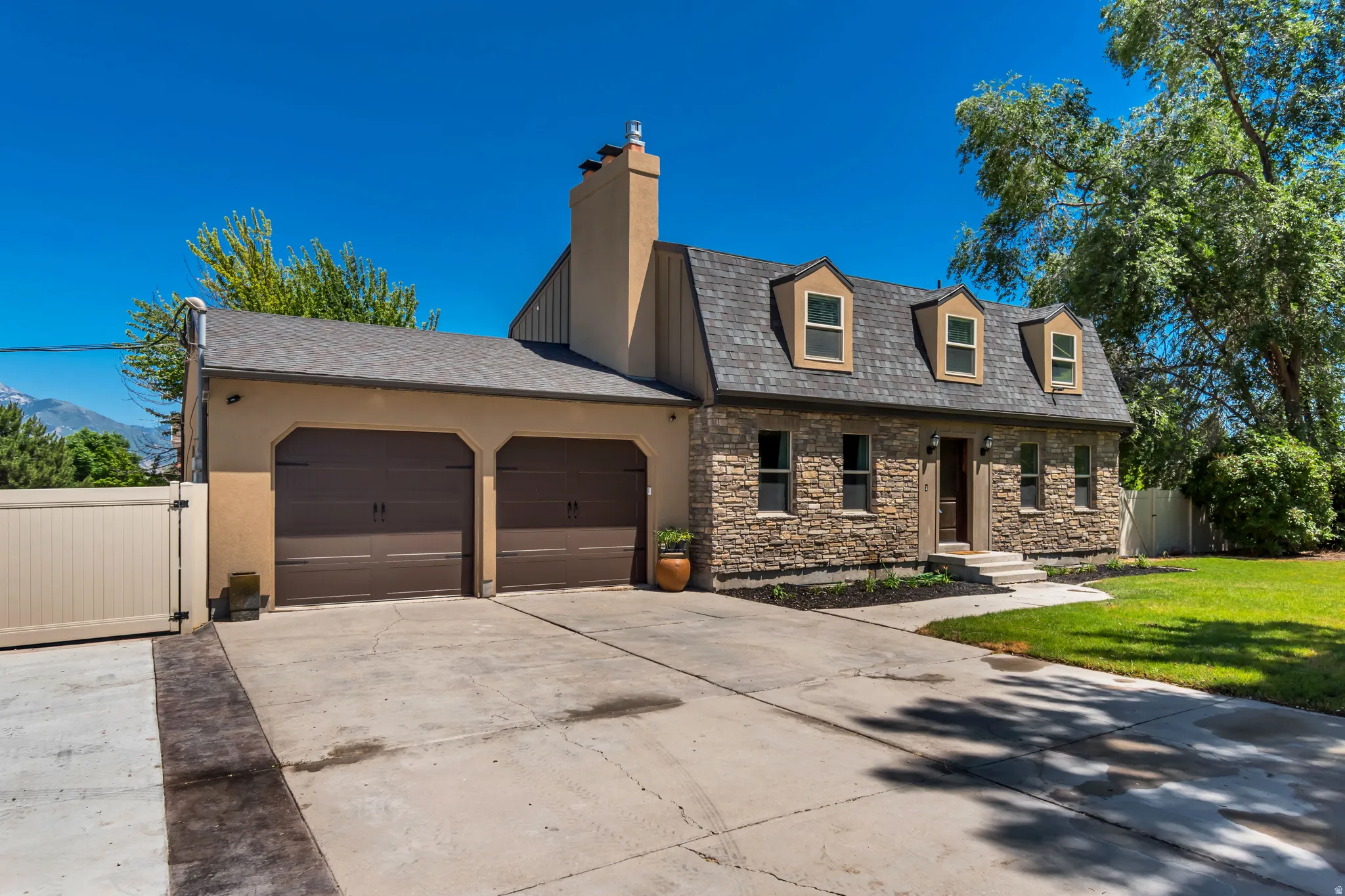 Stone veneer facade with three dormer windows, a two-car garage, and a concrete driveway