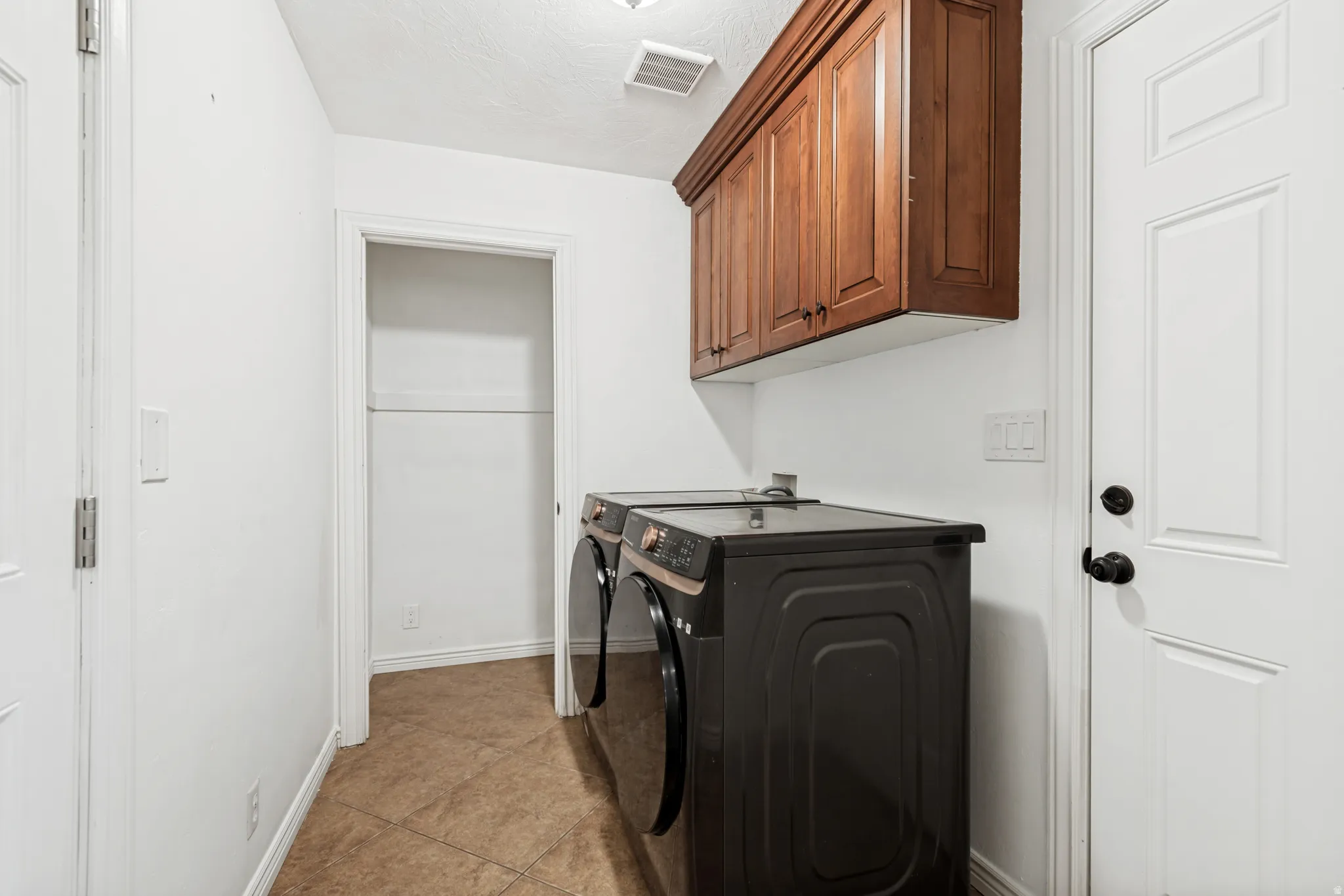 Laundry area featuring rich wood-finish upper cabinetry, tile flooring, and a dedicated storage closet