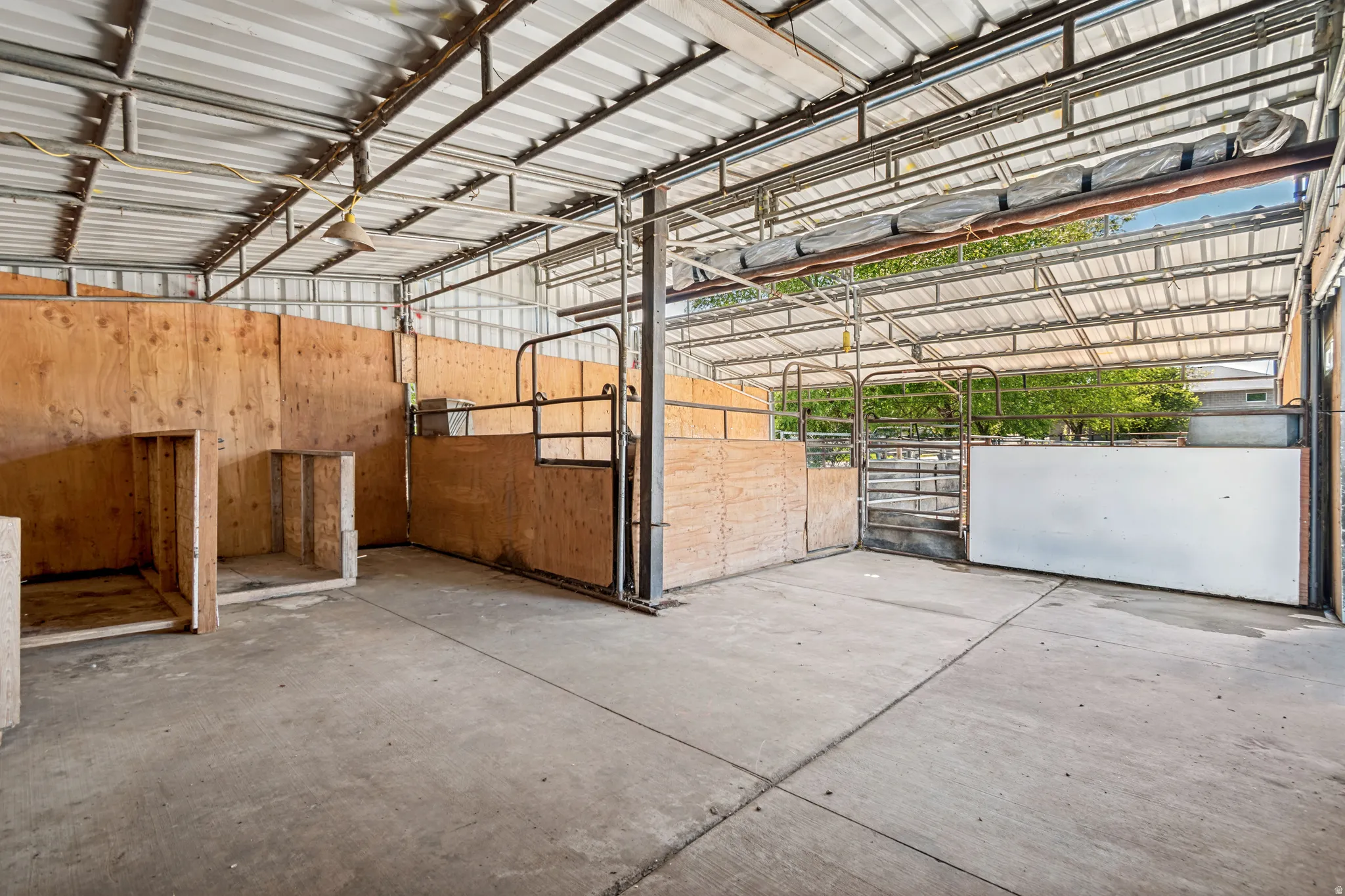 Expansive covered barn structure featuring a concrete floor, metal roof, wood-paneled stalls, and metal gates