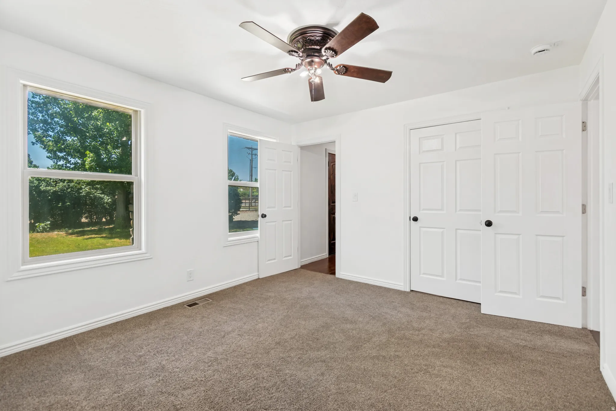Room featuring a ceiling fan with dark wood-finish blades, two windows with white trim, and a sliding closet door with black hardware