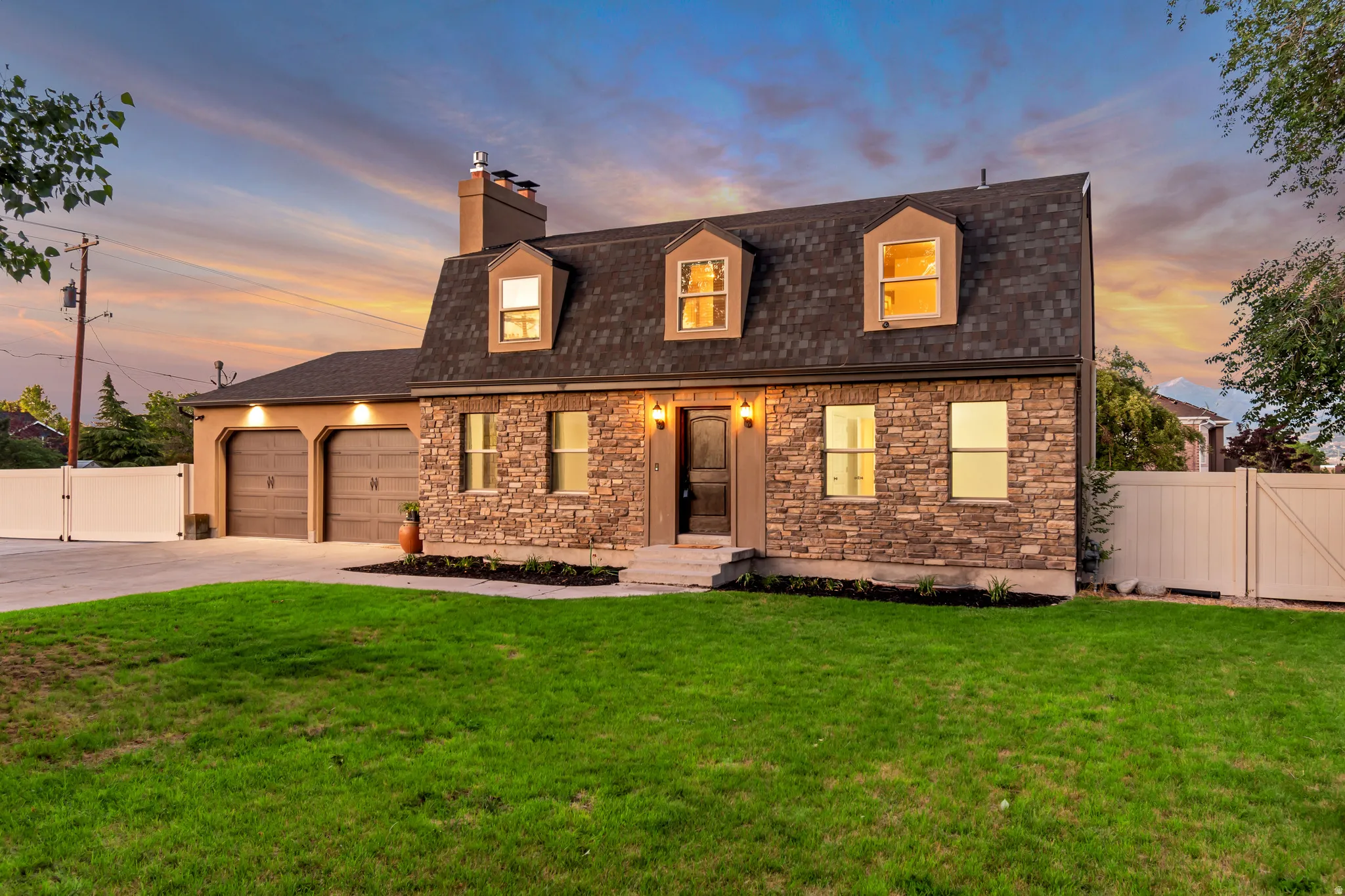 Stone veneer facade with a black shingle roof, featuring three dormer windows and a two-car garage