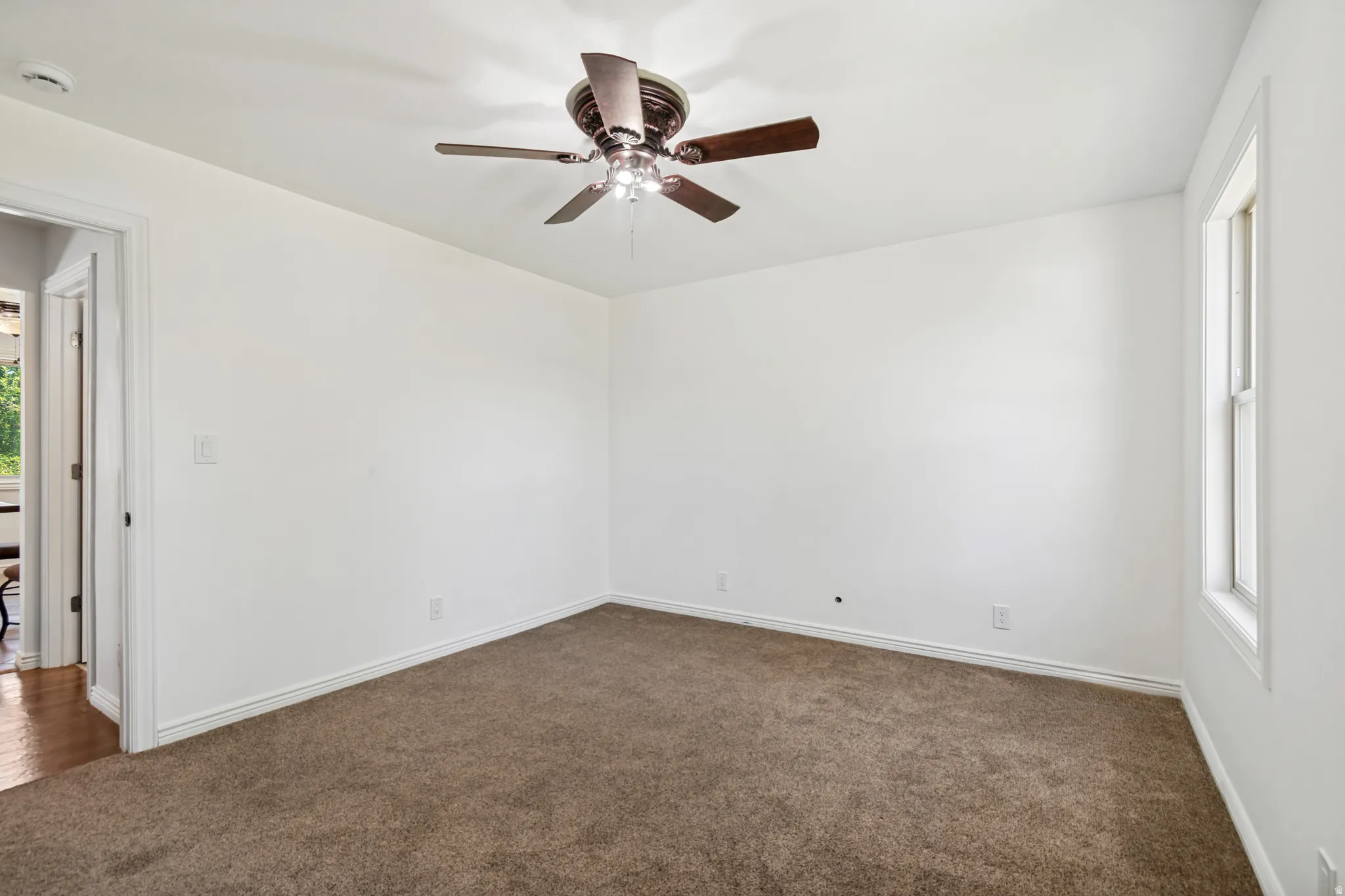 Neutral-toned carpeting grounds this room featuring a ceiling fan with integrated lighting and a window with white trim