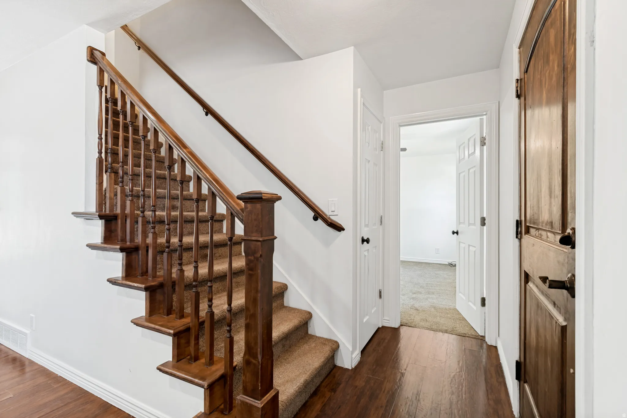 Staircase featuring wood balusters and a carpeted tread, set against white walls