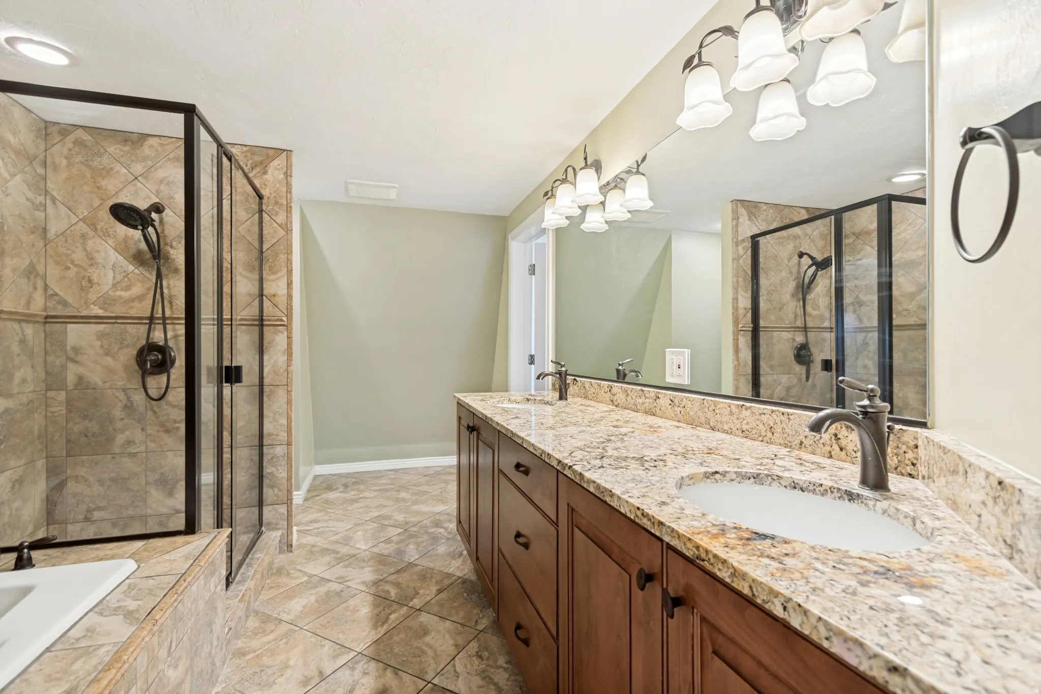 Spacious bathroom featuring a dual vanity with granite countertops, rich wood-finish cabinetry, and undermount sinks