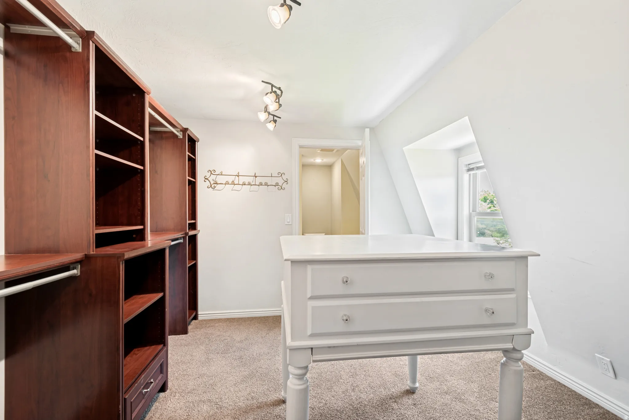 Walk-in closet featuring extensive built-in wood-finish shelving and hanging rods, a central white island with drawers, track lighting, and a sloped ceiling with a dormer window