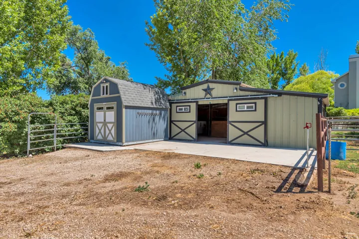 Equestrian facility featuring a multi-stall barn with sliding doors, an attached storage shed, and concrete aprons