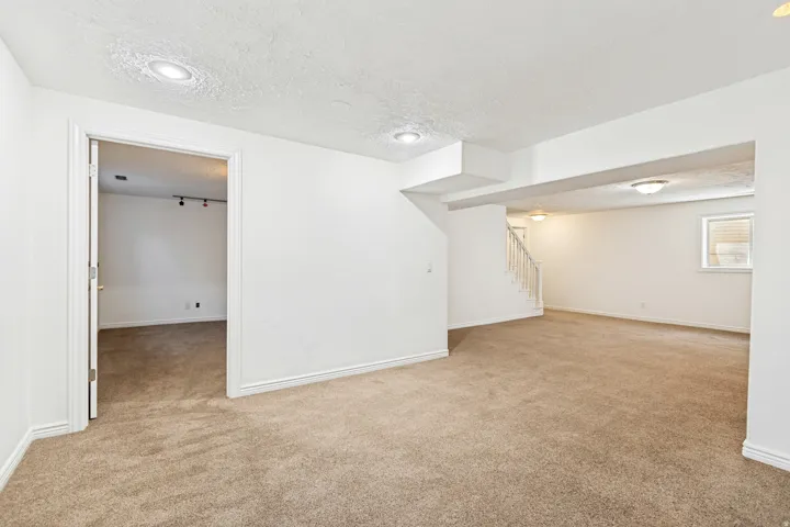 Spacious carpeted room featuring white painted walls, recessed lighting, and a doorway leading to an additional area