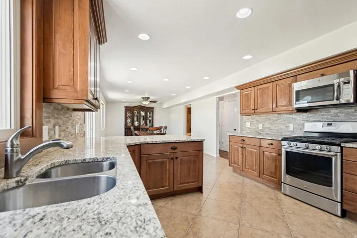 Kitchen featuring wood cabinetry, light-toned granite-style countertops, stainless steel appliances, a double basin sink, and an extended island