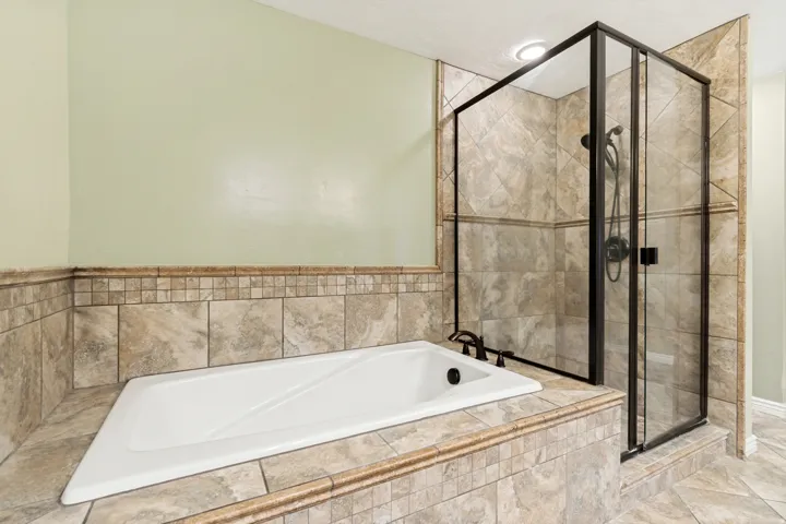 Soaking tub with bronze fixtures, surrounded by neutral-toned tile and a mosaic accent border