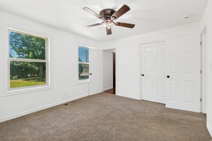Room featuring a ceiling fan with dark wood-finish blades, two windows with white trim, and a sliding closet door with black hardware