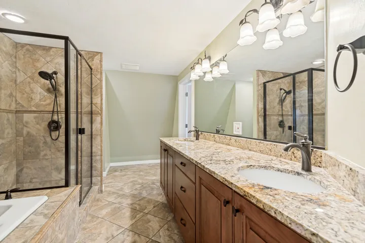 Spacious bathroom featuring a dual vanity with granite countertops, rich wood-finish cabinetry, and undermount sinks