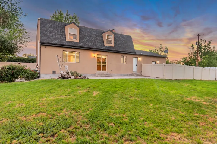 Spacious rear yard with a sloped lawn, stucco exterior, dormer windows, sliding glass door access, and privacy fencing