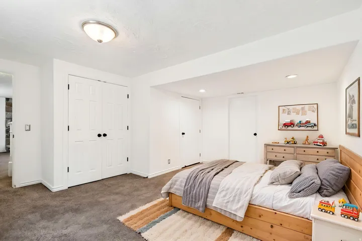 Virtually staged - Carpeted room featuring white walls, a flush-mount ceiling light fixture, and white bi-fold closet doors with black hardware