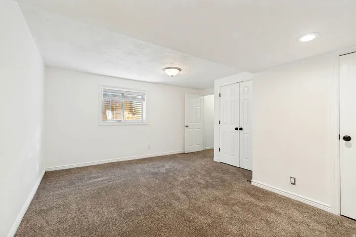 Carpeted room with white walls, a single window with horizontal blinds, and a built-in closet with bi-fold doors