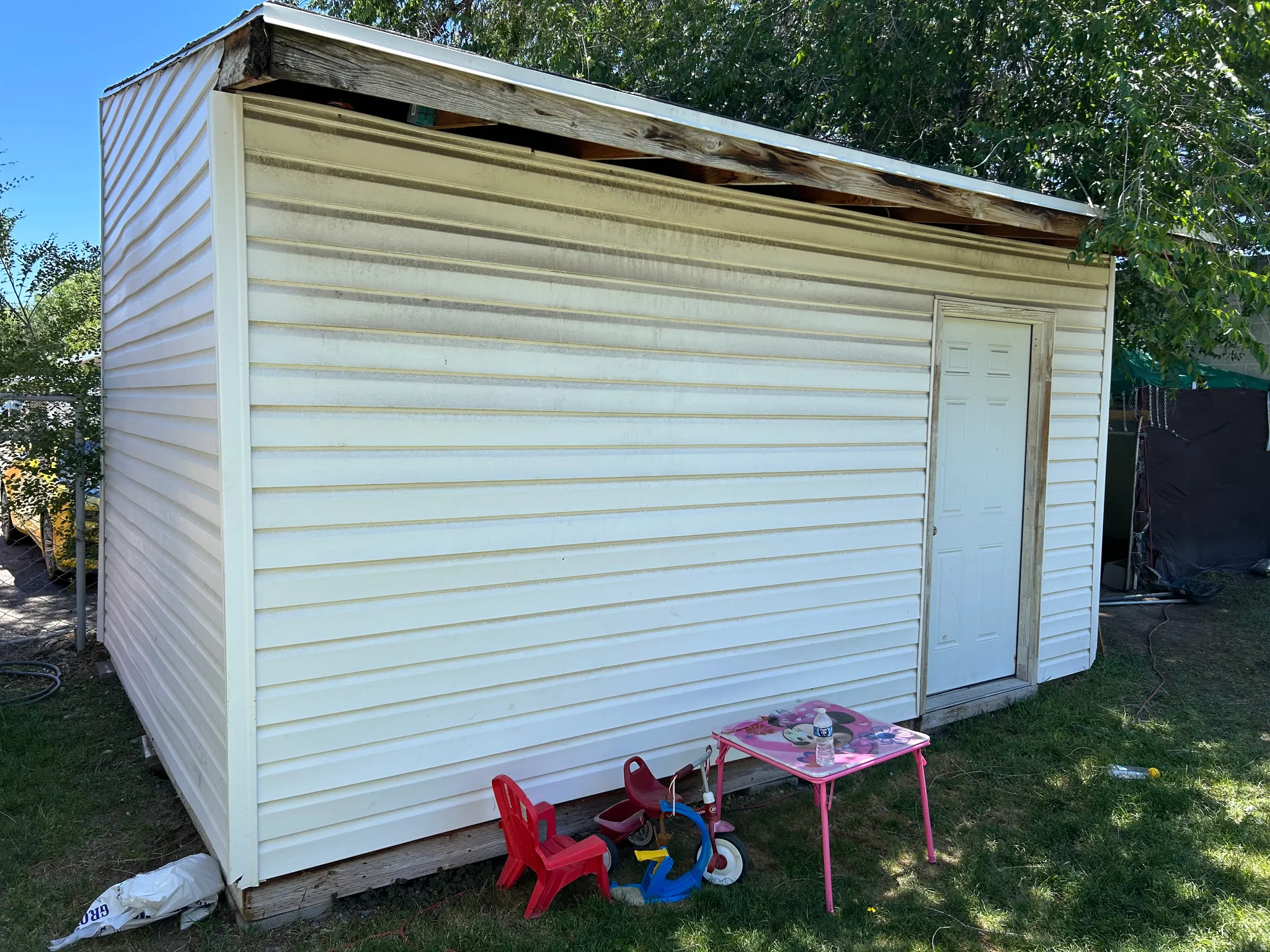 Detached shed with white vinyl siding, a white entry door, and a partially exposed wood roof structure