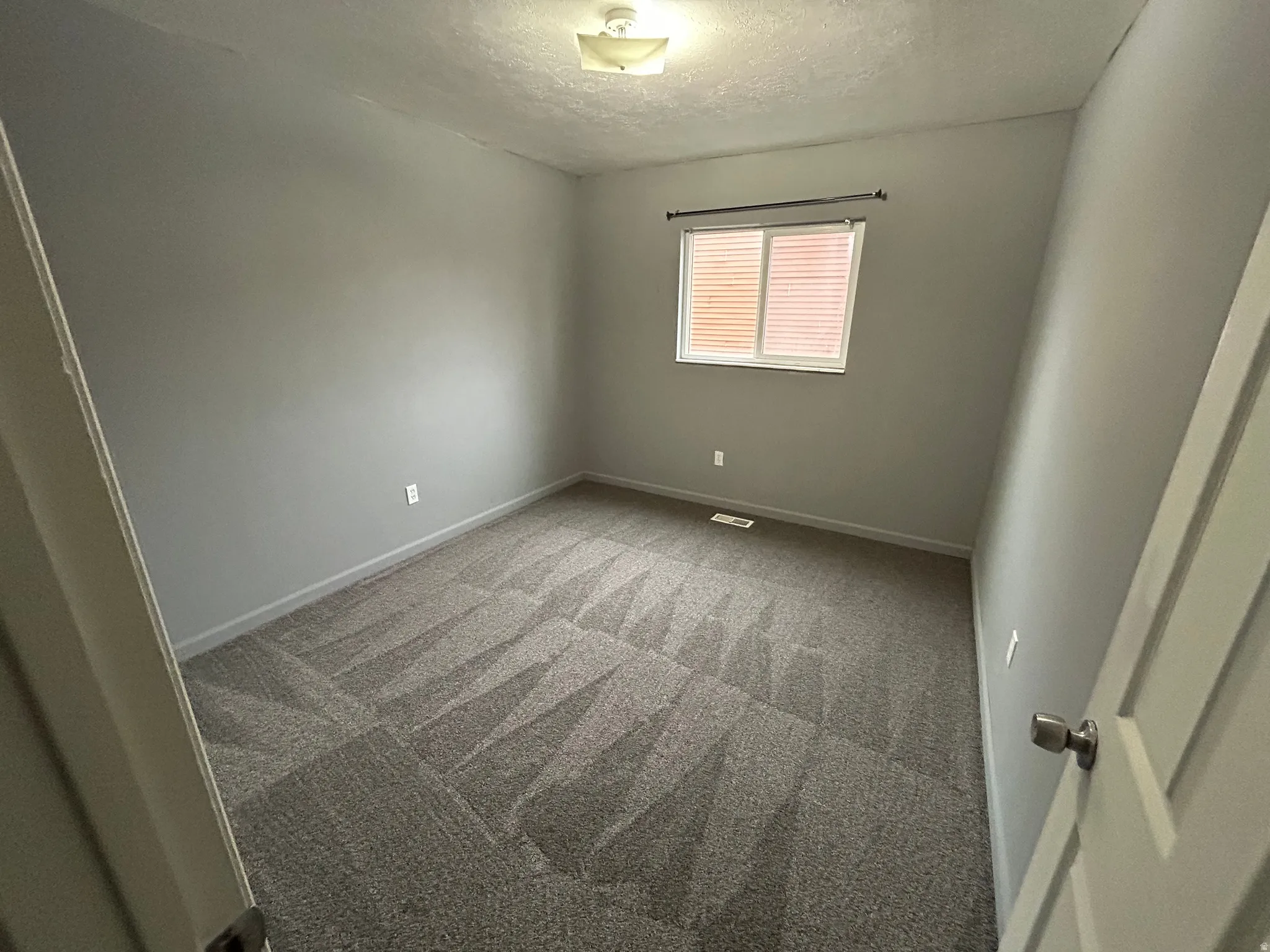 Room featuring neutral gray walls, patterned gray carpeting, and a single window with blinds