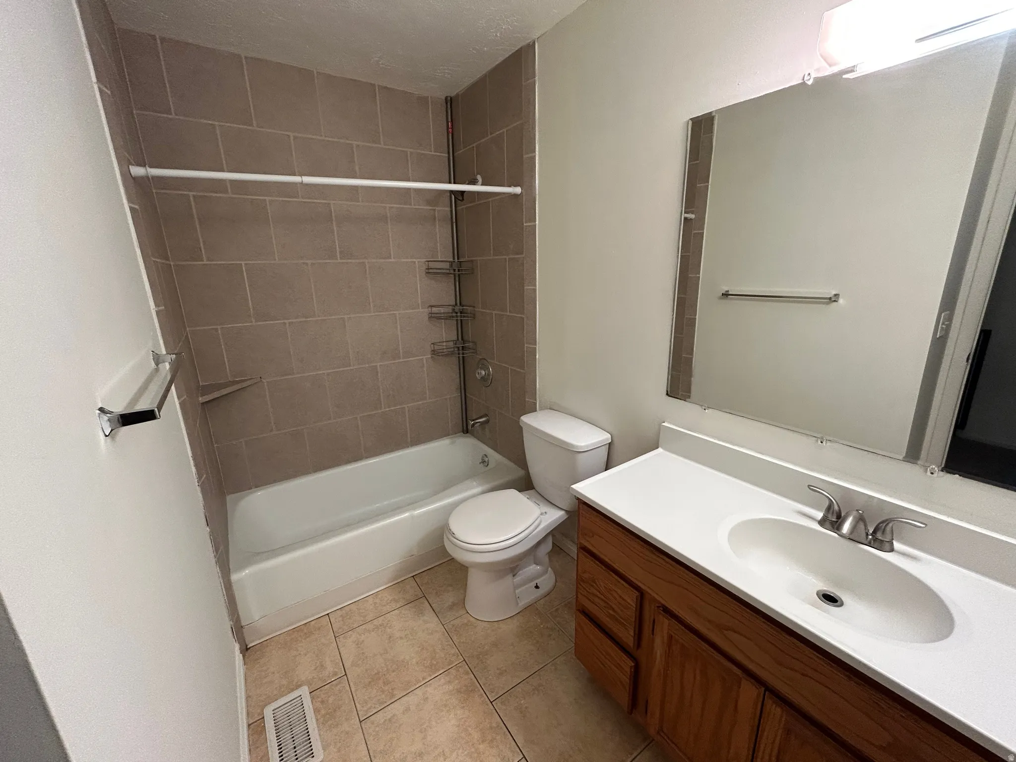 Bathroom featuring a wood-finish vanity with an integrated sink, a rectangular mirror, and a full-size bathtub with tile surround